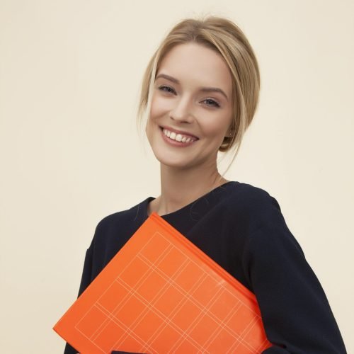 pexels-photo-1587009-1587009 A cheerful woman smiles while holding an orange folder against a neutral background.