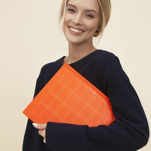 pexels-photo-1587009-1587009 A cheerful woman smiles while holding an orange folder against a neutral background.