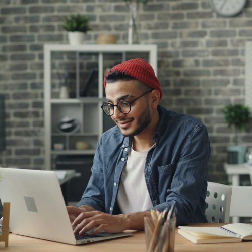 pexels-photo-23496606-23496606 A young man in a beanie working diligently on a laptop in a stylish, modern office space.