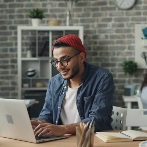 pexels-photo-23496606-23496606 A young man in a beanie working diligently on a laptop in a stylish, modern office space.